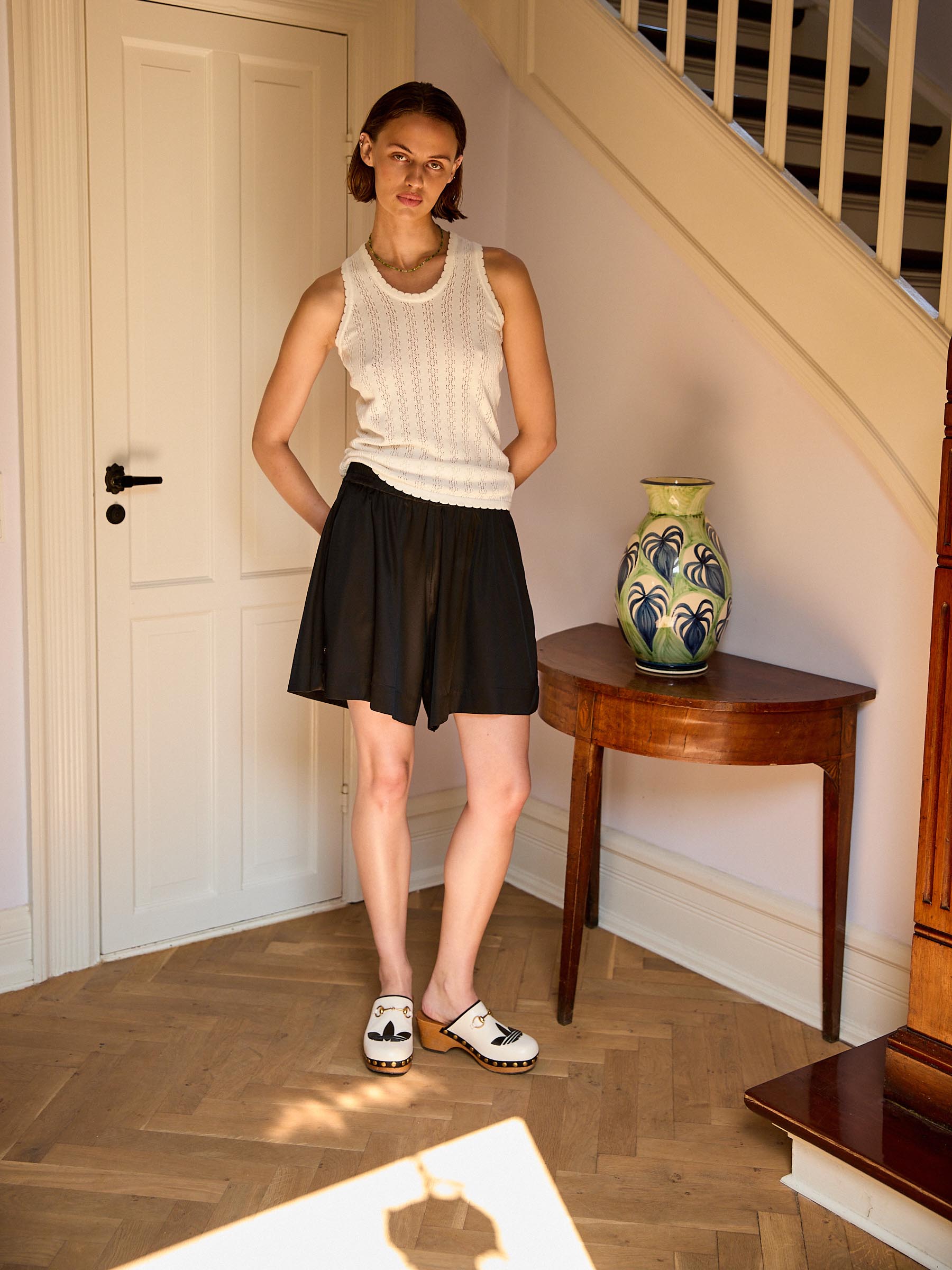 Woman standing in a room with a vase on a table and a staircase in the background